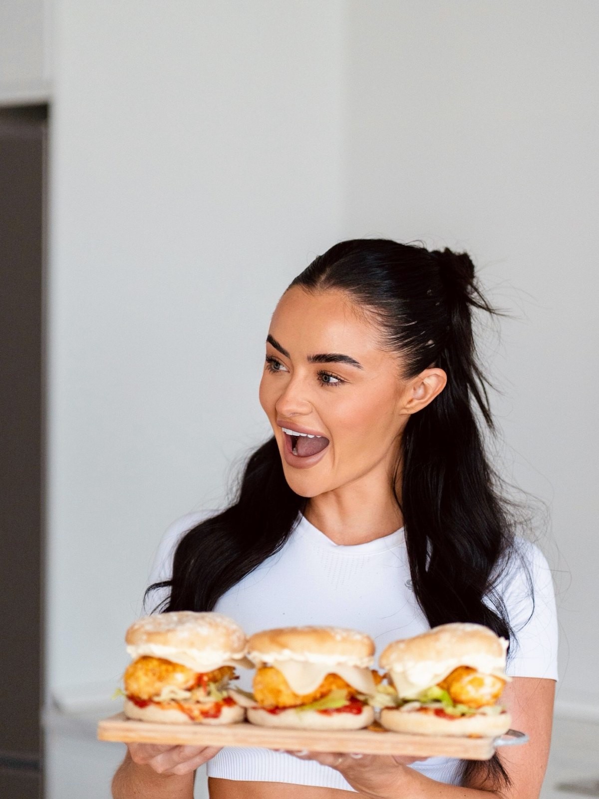 Keelin Nugent laughing in her kitchen holding a board of chicken burgers