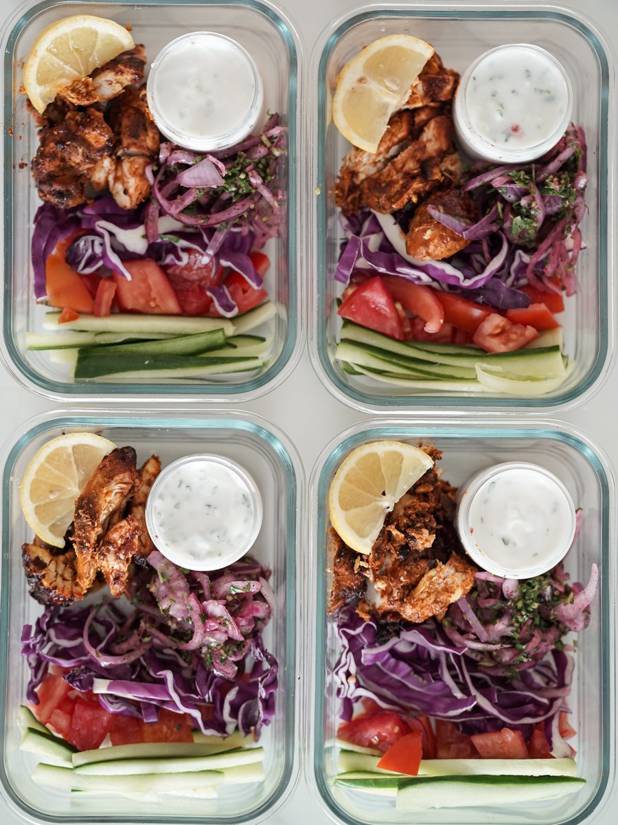 Four glass meal prep boxes of chicken shawarma, each with a small lidded pot of garlic sauce