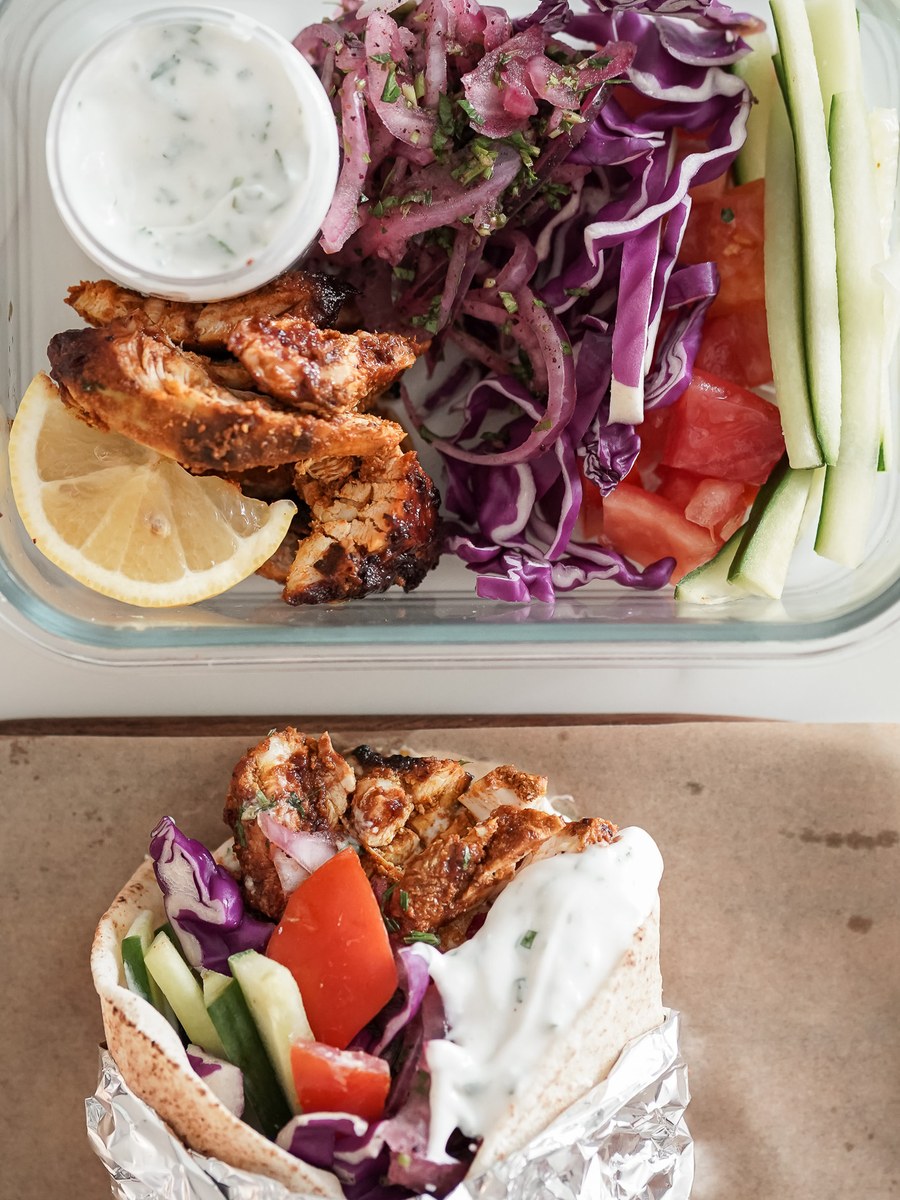 A rolled chicken shawarma wrapped in foil beside its meal prep box