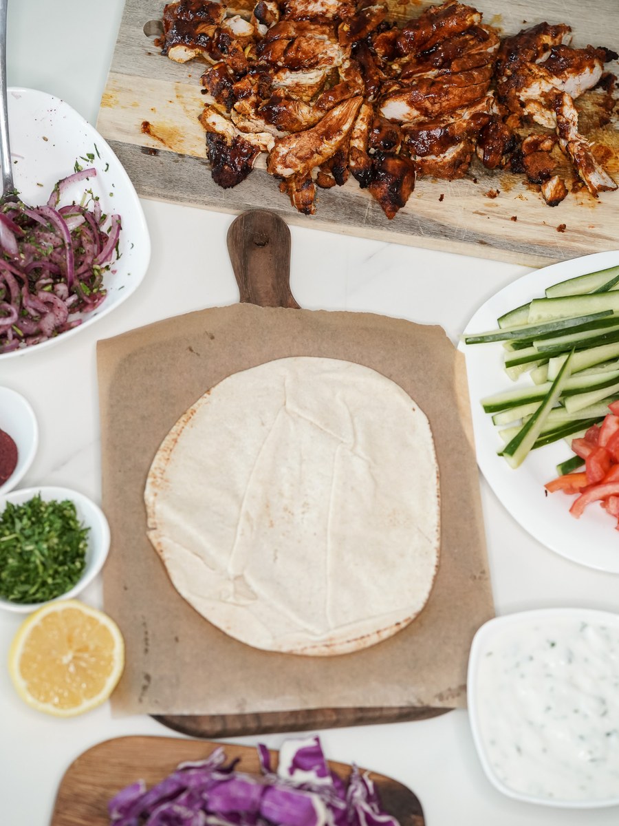 Roast chicken on a board with bowls of sumac onion, cucumber batons, tomato, cabbage, parsley and garlic sauce, laid out ready to box